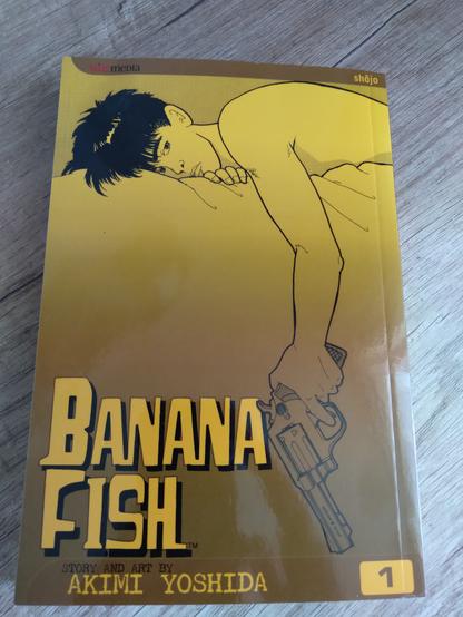 Manga cover of Banana Fish by Akimi Yoshida: a dark-haired young guy lying on his side holding a gun in his hand; background is yellow