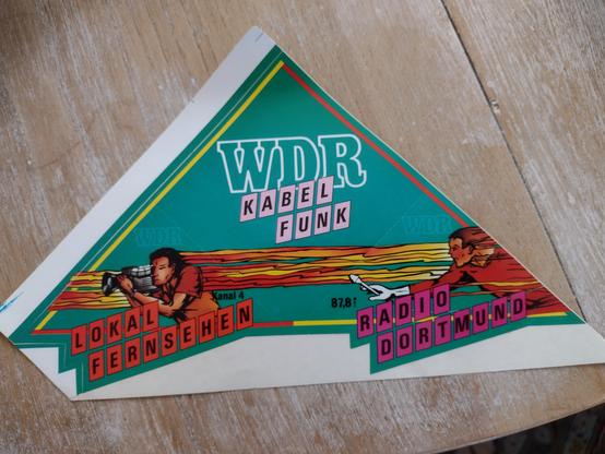 Dreieckiger grüner Aufkleber aus den 1980er Jahren. Aufschrift: WDR Kabelfunk, Lokalfernsehen und Radio Dortmund.