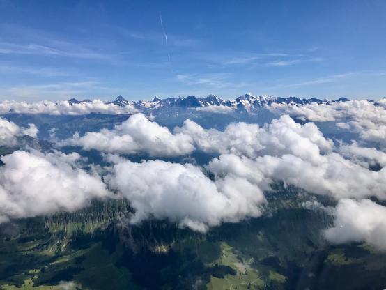 Sicht aus dem Flugzeug in die Schweizer Alpen mit kleinen Quellwolken.