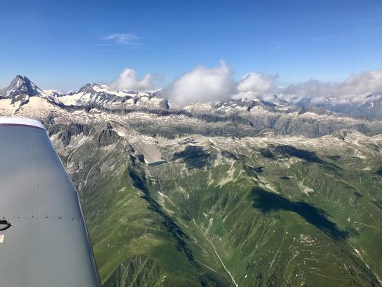 Sicht aus dem Flugzeug in die Schweizer Alpen mit kleinen Quellwolken.