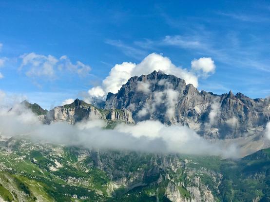 Blick auf Berge in den Schweizer Alpen mit Wolken im Vordergrund und im Hintergrund.