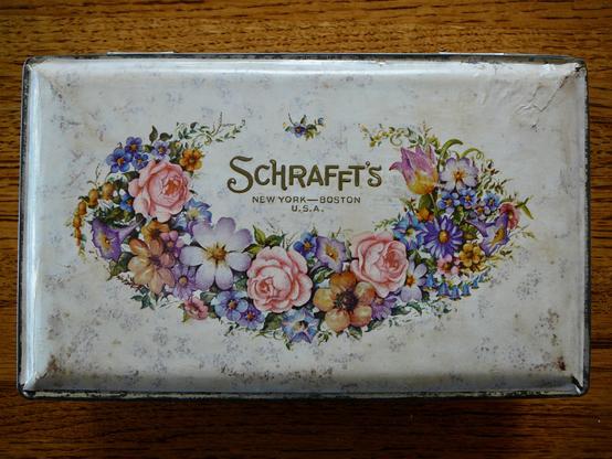 An antiques metal box with a floral pattern that once held Schrafft's Chocolates.