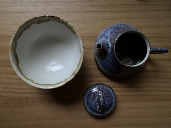 A teacup and teapot with lid with an opal glaze on a wooden table