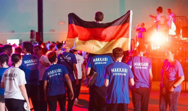 Junge Sportlerinnen und Sportler in blauen T-Shirts mit Makkabi-Deutschland-Aufdruck. Ein Junge sitzt auf den Schultern eines anderen und hält eine Deutschland-Fahne hoch.

Copyright: Makkabi Deutschland / Doctor Lyalya