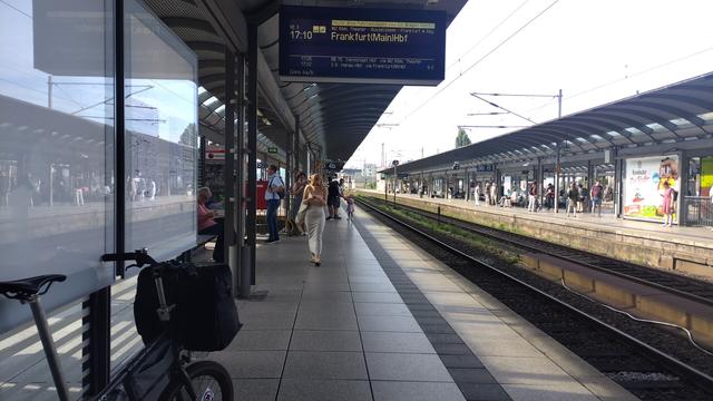 Blick entlang des Bahnsteigs. Auf der Anzeige steht RE 3 mach Frankfurt, darüber als Warnung "Heute ohne Fahrradwagen". Vorn im Bild steht das Faltrad mit Packtasche vorn drauf.