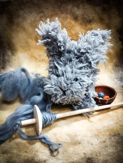 A photo of a toy bunny and a drop spindle with some yarn.