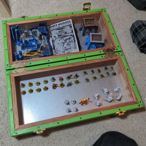 The inside of a travel gaming set filled with scenery, miniatures and even a tiny copy of the space weirdos rule book.