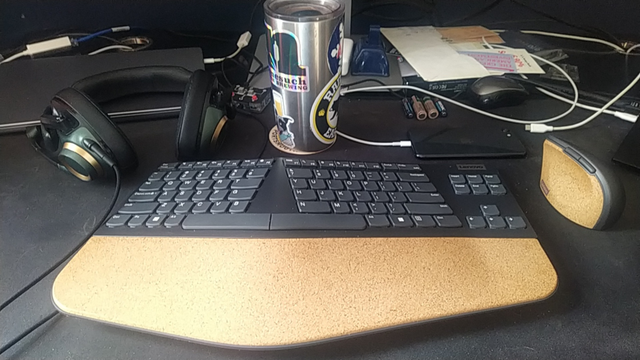 An ergonomic keyboard and mouse on a giant mousepad desk. The desk is kind of a mess too.