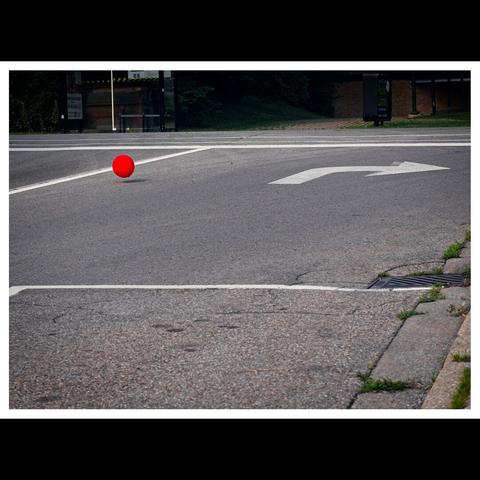 Red balloon bouncing down an empty road.