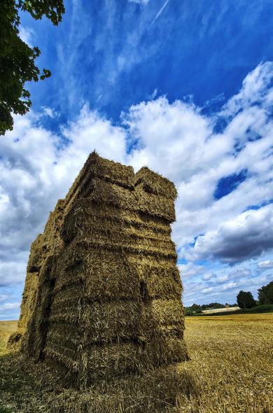 a giant pile of hay bales under puffy clouds in the sky