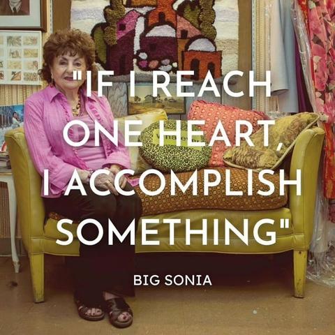 Photo of elderly Sonia Warshawski, looking smart in a pink blouse, dark slacks and slides. She is seated on a small sofa covered in colorful cushions. Text over the image says: "If I reach one heart, I accomplish something. - Big Sonia."