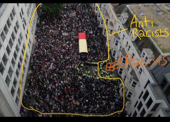 Photo of demo.  Yellow line drawn around the large numbers of anti fascists and an arrow pointing to the few fascists behind the high vis jackets of Police keeping them apart.