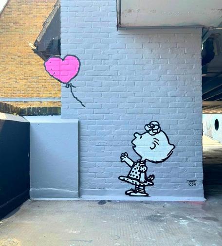 Streetartwall. A mural based on Banksy's "Girl with Balloon- Serie" was sprayed onto a gray brick wall in a parking garage. The mural was created using stencils in the colors black, white and pink. The little girl is "Sally" from the Peanuts comic series. She is depicted in black and white in a dotted short dress and is holding out her hand for a pink, heart-shaped balloon that is being carried away by the wind. 
Info: Sally Brown is the sister of Charlie Brown. A blonde girl with a pink polka dot dress. Sally is inquisitive and demands an answer for everything. She is the annoying little sister.