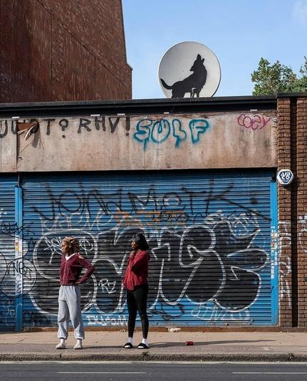 Streetartwall. A new work by Banksy has appeared on an old round TV satellite system. The satellite system stands above a long, low building with a rolling gate covered in graffiti. It shows a black wolf howling at the moon (the satellite system).The photo shows two innocent passers-by standing unknowingly in front of the roller shutter.
Note: I am not aware if the installation has already been on site. A context has not yet been published. 08.08.2024. Four days, four Banksys...