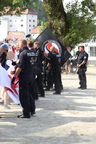 Eine Polizeikette bemüht sich die antifaschistische Gegendemo zurück zu halten, im Hintergrund eine große schwarze Fahne der Antifaschistischen Aktion