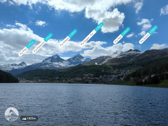 Panorama of Sankt Moritz, through the lake, with moutain peaks marked on it. It's a chilly summer day, about 16 degrees and windy, there's still a lot of snow on the mountains in the background.