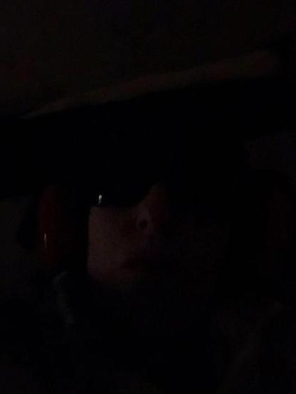 Very ill woman in bed in dark room with ear defenders and sunglasses to reduce sensory overload.