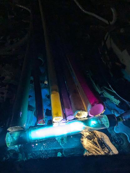 Eight tubes being illuminated by a little quartz glass argon mercury germicidal bulb. My batteries were running low on my tube checker- So I hooked the tube up to the aging transformer. VERY excited for that pink. Slightly scared and mystified that my wiping the phosphor off my glove on the table actually glows :)
