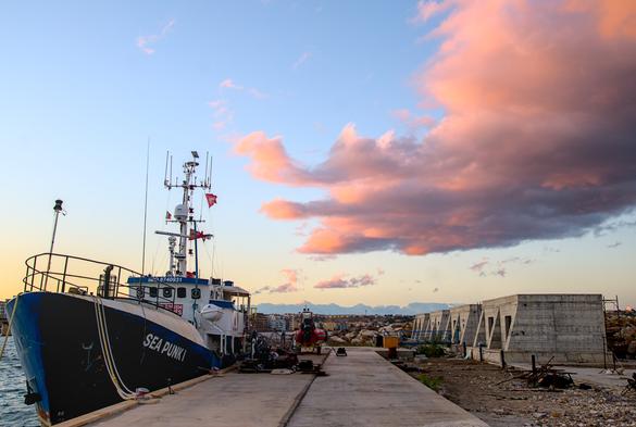 das rettungsschiff "Sea Punk 1" liegt am pier in august/italien. wie wolken am himmel färeben sich rosa/pink durch den untergang der sonne.