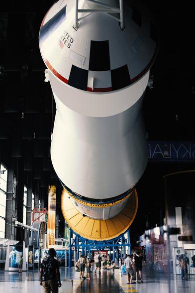 Massive rocket hung horizontal above the floor of a big museum, with people walking underneath it.
