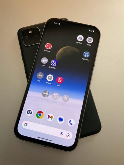 A Pixel 8a shows grayed-out icons for apps that have not yet been installed, with the Capital Bikeshare app in mid-install. That phone rests on top of a dead Pixel 5a with its back camera facing up.