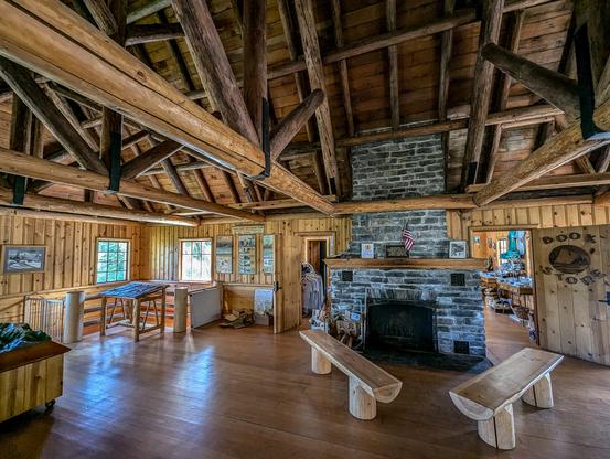 Interior space of the Heather Meadows Visitor Center. At the back wall is a large stone fireplace. The walls are paneled in knotty pine. The ceiling is exposed timbers of round logs. The floor is polished wood planks.