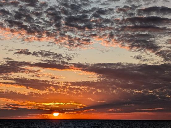 Dramatische Farben - orange, durchsetzt von schwarzen Schäfchenwolken - bei untergehender Sonne über dem Meer.