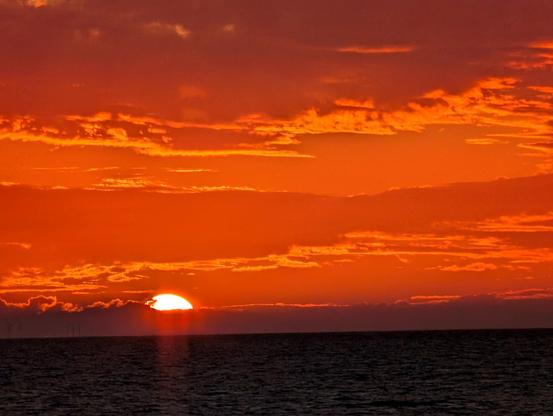 Unten Meer, wenig, etwas 1/7 des Bildes, fast schwarz. Darüber intensives Orange. Die untergehende helle Sonne ist nur noch zu einem Drittel zu sehen