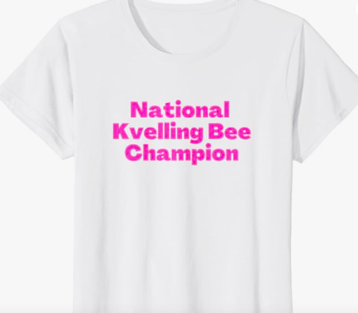 The funny Yiddish National Kvelling Bee Champion is shown in pink lettering on a T shirt.