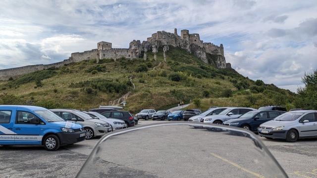 View from the motorcycle half through the wind shield, standing in the parking place under a castle on a nearby hill, cars parked on the side of the picture.
