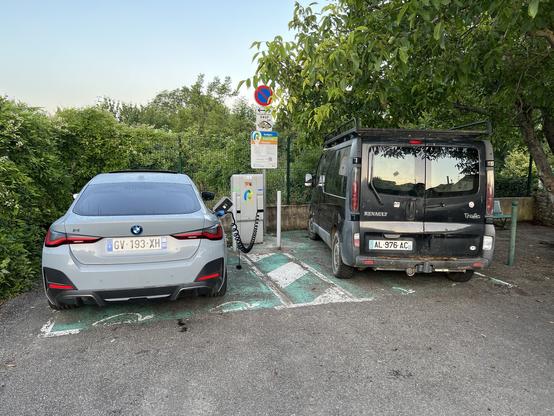 Two parked cars beside a charging station, one is an electric BMW i4 sedan and the other is a Renault ICE van.