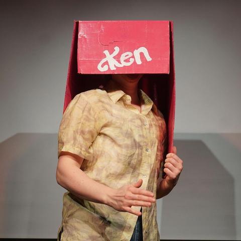 Person in pink cardboard packaging saying "Ken" in white letters at the front.