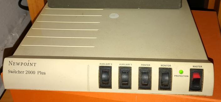 Photograph of a working Newpoint Switcher 2000 Plus power switch. It has four power switches, two are flipped on. It is a short rectangle shape, allowing it to also serve as a monitor stand.