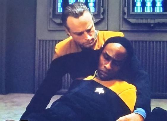 Lon Suder in yellow enterprise uniform holds an unconscious Tuvok.