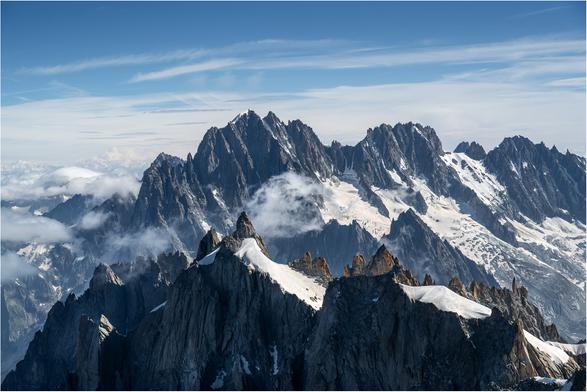 The jagged ridge line of the foreground peaks set against the background peaks of the Aiguille Verte. Blue skies and snow.