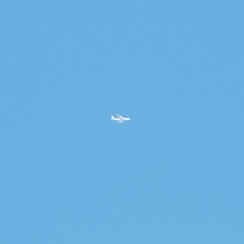 A small white airplane flying against a clear blue sky. It is a four engine jet.