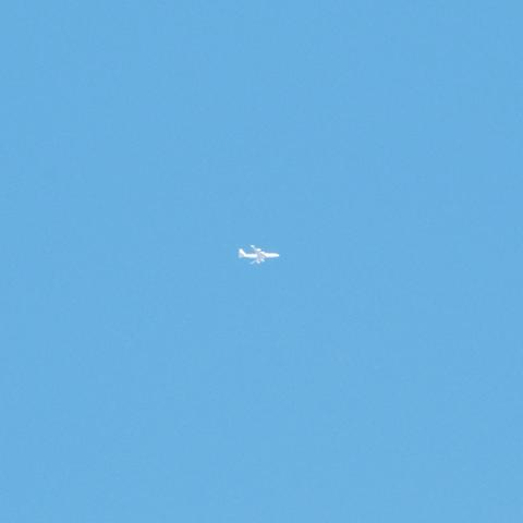A small white airplane flying against a clear blue sky. It is a four engine jet.