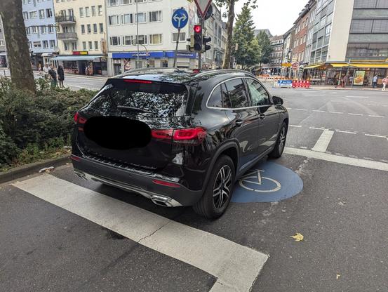 Ein schwarzer SUV steht komplett auf der aufgeweiteten Radaufstellfläche eines benutzungspflichtigen Radwegs.
