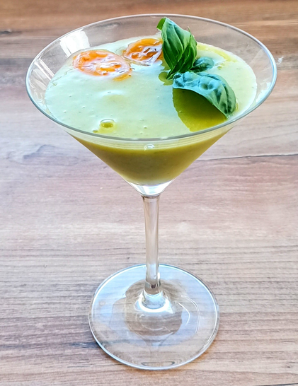 ein Gelbgrüner dickflüssiger Cocktail in einem Martiniglas, dekoriert mit 2 Scheibchen von gelben Tomaten und Basilikum