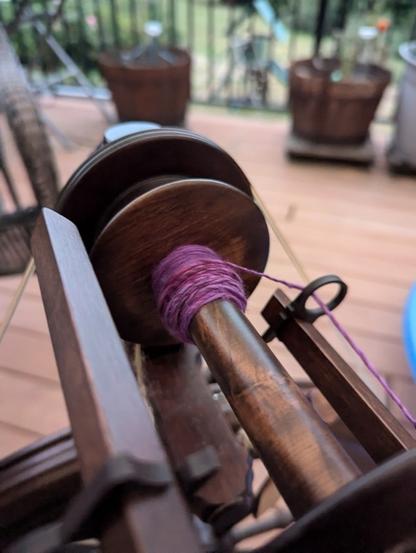 A very small bump of yarn on my wooden spinning wheel sitting out on the deck. The fiber is purple and I'm spinning thinner than I did for my last sample.
