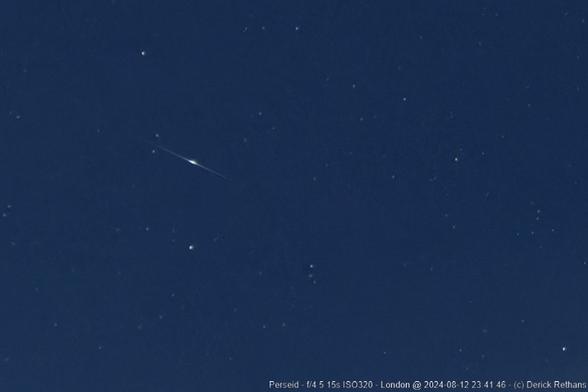 A dark blue night sky, with a bunch of stars. In the bottom left third, there is a shooting star: a middle bright bulb, with a streak on each side.

A description in the bottom right says:
Perseid - f/4.5 15s ISO320 - London @ 2024-08-12 23:41:46 - (c) Derick Rethans
