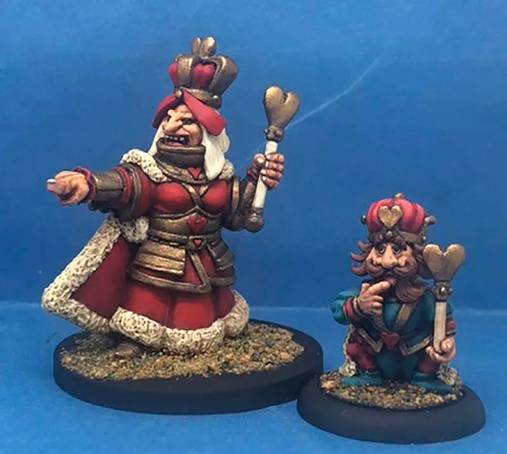 A pair of intricately painted miniatures depicting the Red Queen and her king from the Alice in Geründerland chess set. The Red Queen is depicted as a larger, imposing figure in a red and gold robe, wielding a sceptre and pointing with authority. Beside her, the king is smaller, with a bemused expression, holding a smaller sceptre, both standing on textured bases against a blue background.