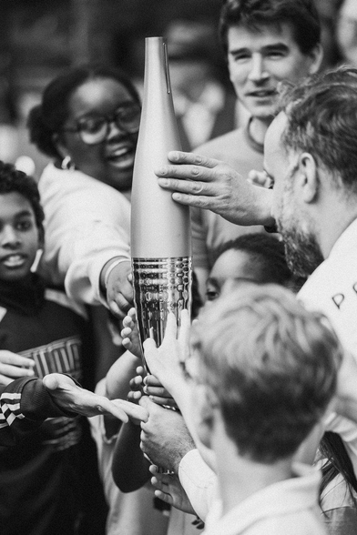 Des enfants et jeunes français touchent la flamme olympique, portée par Arthur Dénouveaux devant la salle de concert "Le Bataclan".