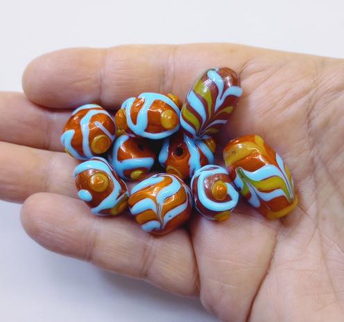 A handful of handmade lampwork glass beads with feathering and dot surface decorations, part of an ongoing project.
