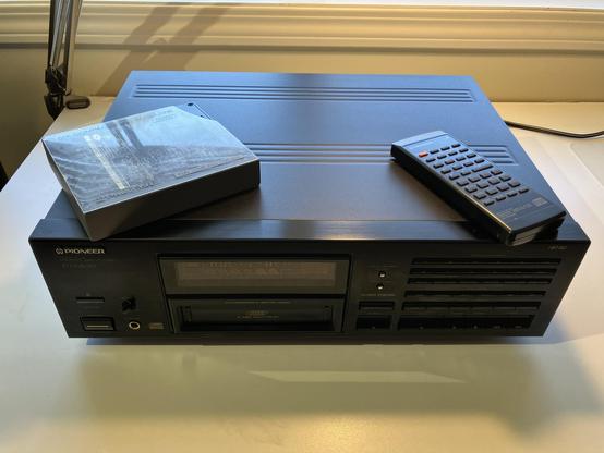A black Pioneer PD-M650 CD player with a six-CD changer cartridge and a remote control resting on top. The cartridge is labeled "Six-Compact Disc Magazine" and designed for home and car use.