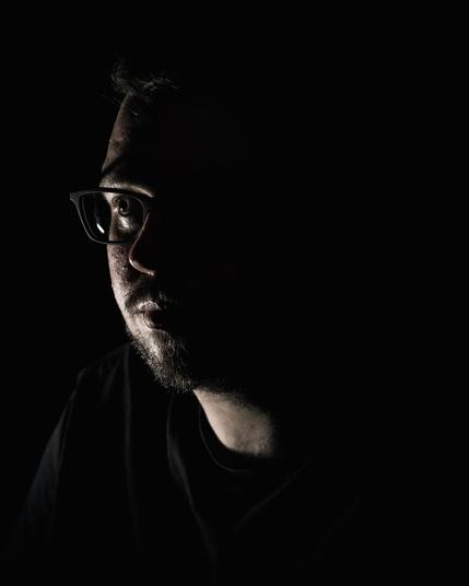 A man lit only from one side looks off to the side of the camera.
