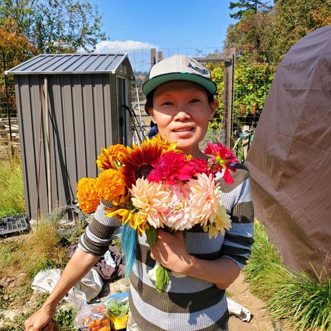 Photo of me at the farm, holding 2 different flower bouquets in my left hand. Dahlias & sunflowers.