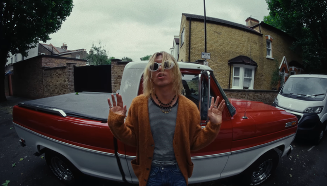 Colde paying respect to Kurt in the Nirvana Blues MV. He's wearing the signature white sunglasses, the messy bleached hair, the cardigan, the striped shirt. Standing in front of a pickup truck (but on a London Street!).