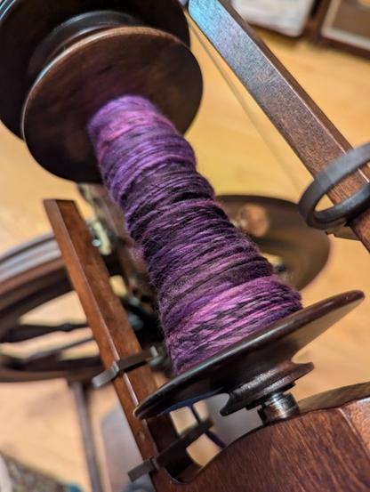 Some purple tonal fiber spun into a single of yarn on a wooden bobbin.