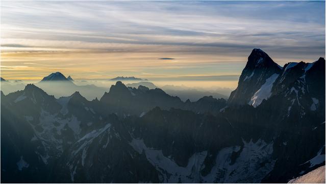 Early morning colours illuminate layers of jagged peaks. On the far right lies the conical outline of the Grand Jorasses.